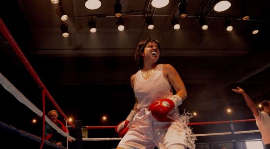 Female boxer with messy brown hair, red gloves, white mouthpiece and all-white outfit standing proudly in the ring and kinda roaring.
