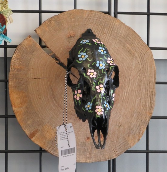 Deer skull hanging on a wall, painted black with flowers on it.