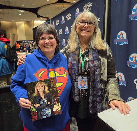 Anne posing with Karen Allen at her table while holding an autographed 8x10, both smiling very sweetly.