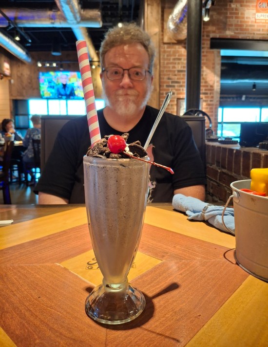 Me sitting behind a chocolate shake in a tall glass.