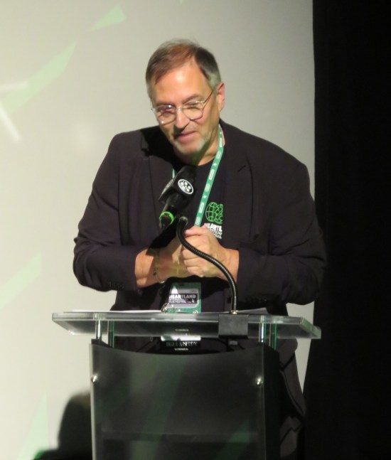 Michael Ault at a glass podium next to a movie screen.