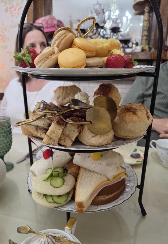 Three-level black metal serving tower filled with macarons, fruits, cakes, and tiny sandwiches.