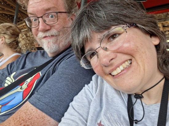 Anne snapping a selfie of us. Her shirt is blue-and-white stripes, mine is gray and has Vault Boy on it. We're both smiling and the top of my head is cut off.