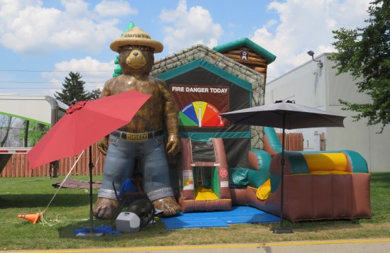 Cabin-shaped bounce house with an inflatable Smokey the Bear standing guard and a fake "Fire Danger Today" gauge over the entrance flaps.