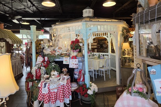 White gazebo with table and chairs inside it, all in a large indoor space. Other tables offer tea-related accessories for sale.