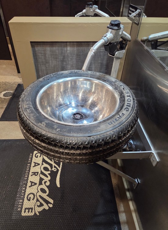 Sink that's a metal bowl inside a tire, faucet shaped like a gas pump, and a Ford's Garage floor mat.