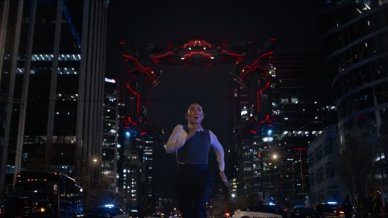 Greta Lee in a police vest running away from a giant neon-red Recognizer down a generic city street.