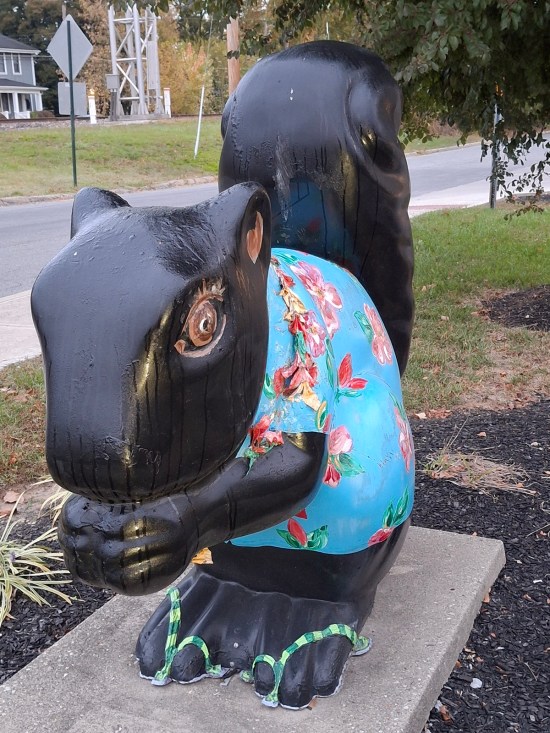 Statue of a gray squirrel gnawing on an acorn and wearing a blue tropical shirt.