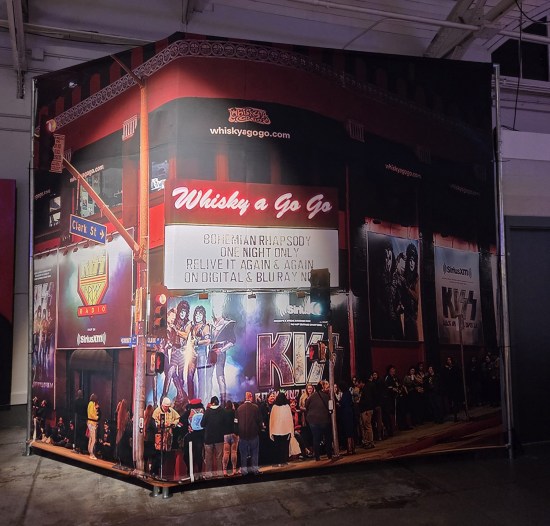 Floor-to-ceiling Whiskey a Go Go cardboard facade, photographed at nighttime. The marquee boasts a screening of the film Bohemian Rhapsody.