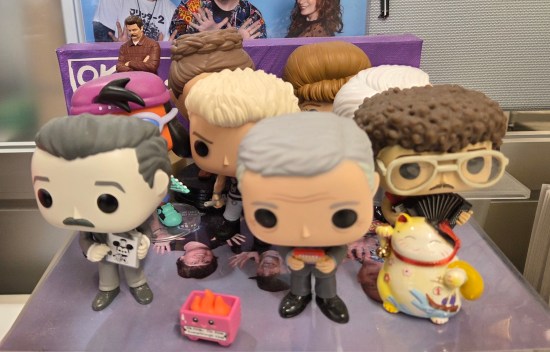Several Funko Pops on a cubicle shelf. Front row is Walt Disney, Alex Trebek, and Weird Al.