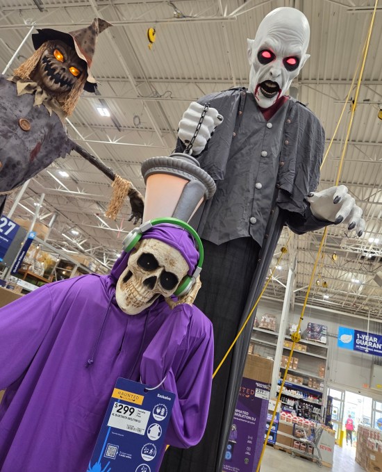 Tall Halloween yard animatronics for sale in a hardware store, all over six fee tall: ghoul, purple robed skeleton and scarecrow.