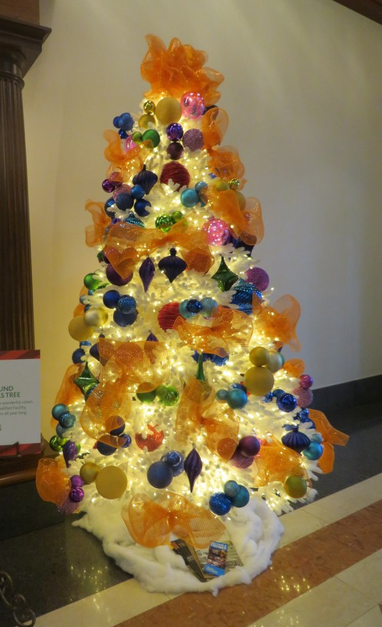 white Christmas tree with orange netted garland and mostly blue ornaments
