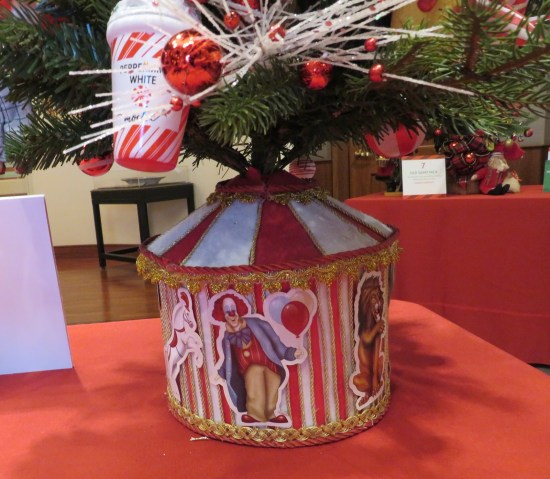 Circus-themed  bucket holding a miniature Christmas tree. Center image looks kinda like Pennywise from Stephen King's "IT".