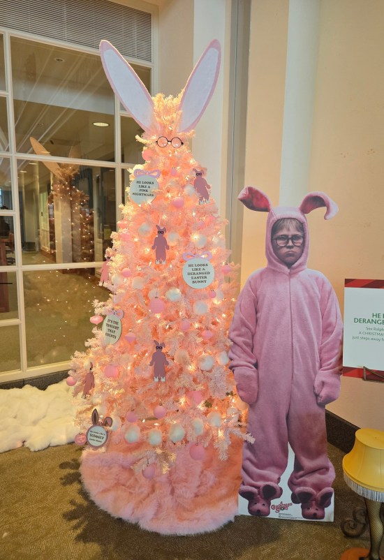 Pink and white Christmas tree with Ralphie ornaments and bunny ear topper. Next to it is a cardboard standee of Ralphie in bunny suit from "A Christmas Story".