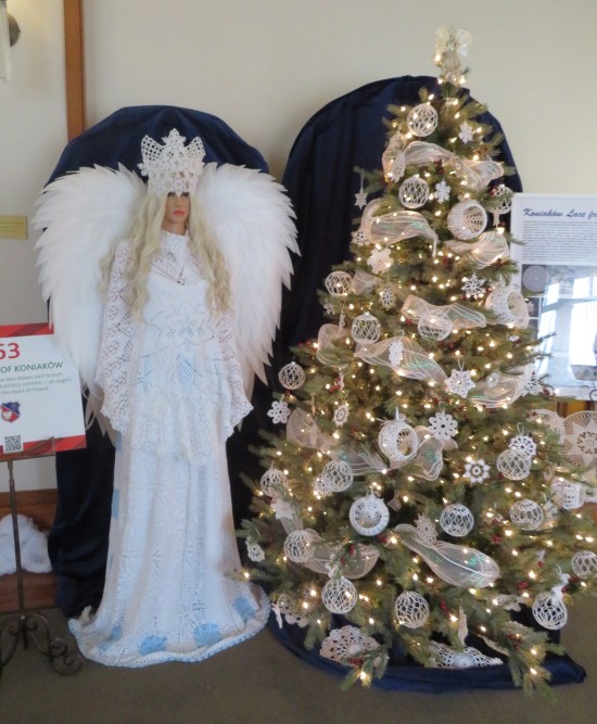 light green Christmas tree with all white mesh ornaments. Standing next to it is a blond mannequin dressed like an angel.