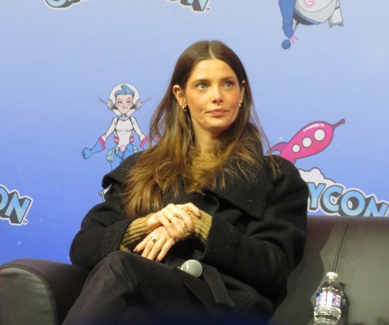 Ashley Greene patiently sitting on a stage, dressed in all black.