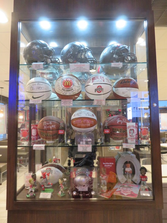 Large glass display case with football helmets and basketballs.