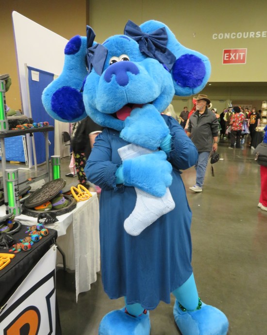 Blue cosplay, giant mascot size, holding an all-white Christmas stocking.