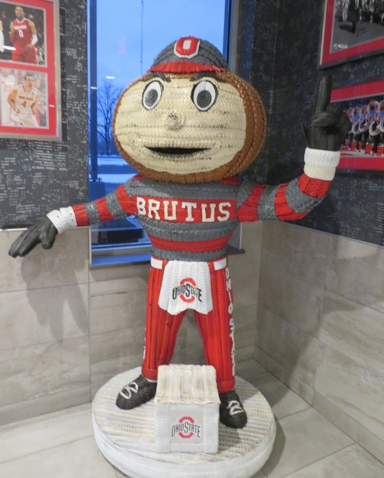 Statue of a red and gray college sports mascot with a buckeye nut for a head, standing in the corner of a McDonald's.