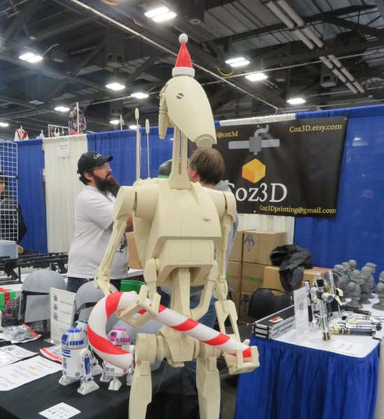 Lfe-size Battle Droid statue with Santa hat holding a big candy cane instead of a blaster.