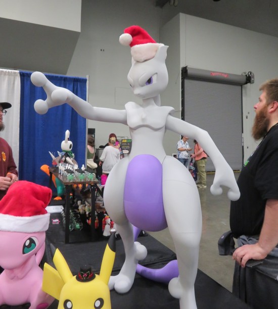 Large Pokemon Mewtwo statue on a dealer table with a Santa hat on its head.