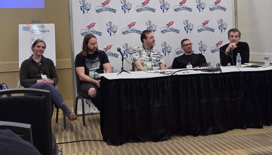 Four comics writers and a moderator at a white table draped in black.
