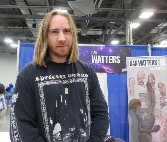 Dan Watters at his booth in a long-sleeved Spectral Wound shirt and a bloodied banner for "The Six Fingers".