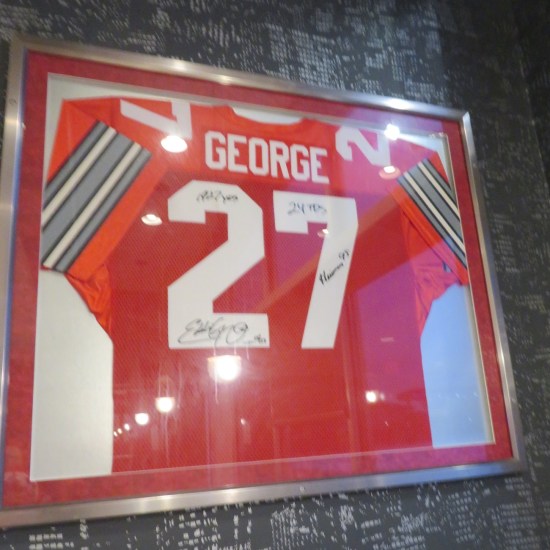 Red jersey with white number 27 and autographs, encased in glass on a restaurant wall.
