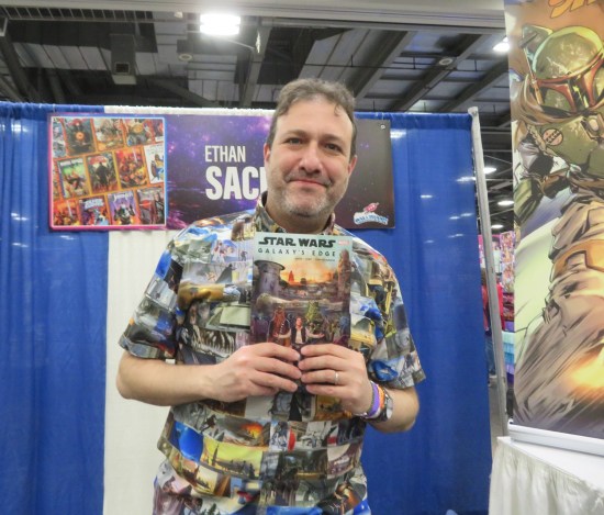 Ethan Sacks at his booth, holding a copy of "Star Wars: Galaxy's Edge".
