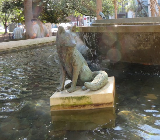statue of a sitting fox surrounded by water in the middle of a city fountain