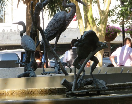 A frog statue leaping, in front of multiple flamingo statues