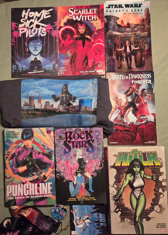 Six graphic novels, an omnibus, a Godzilla T-shirt, a button and a flimsy cardstock con badge.