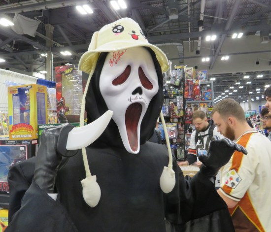 Mannequin at a dealer table dressed with Ghostface mask, black robe, anime fishing hat and stabby knife.