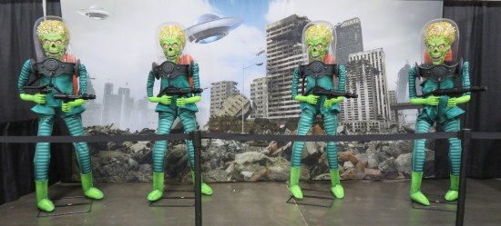 Statues of four aliens from "Mars Attacks!" in front of a backdrop of some major city crumbling.