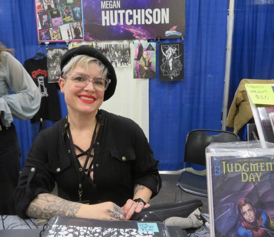Megan Hutchison at her booth in glasses, tattoo, and black beret.