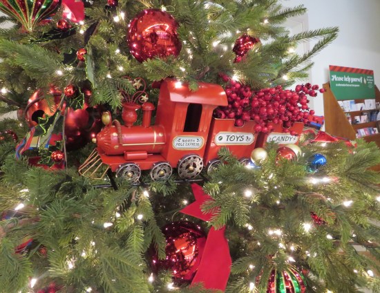 red wooden train resting on several branches of a decorated Christmas tree.