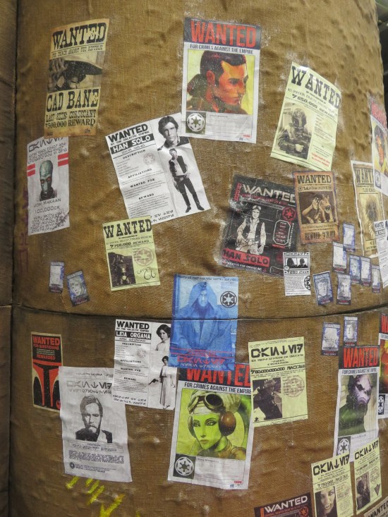 Large brown column covered with WANTED posters for various Star Wars characters.