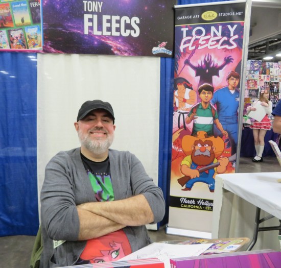 Tony Fleecs sitting at his booth, arms crossed.