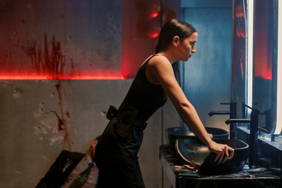 Ana de Armas wears all-black action-hero clothing in a fancy nightclub bathroom where a bloody corpse has slid down the far wall.