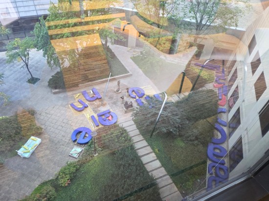 Courtyard with trees, bushes, and giant blue letters lying around the walkways.