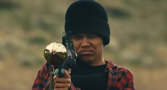 Teyana Taylor wearing black winter cap and red-and-black flannel, aiming a grenade launcher.