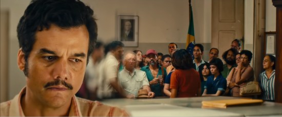 Closeup of Wagner Moura's face as he decides whether or not react to a specific customer among a crowd in an office.