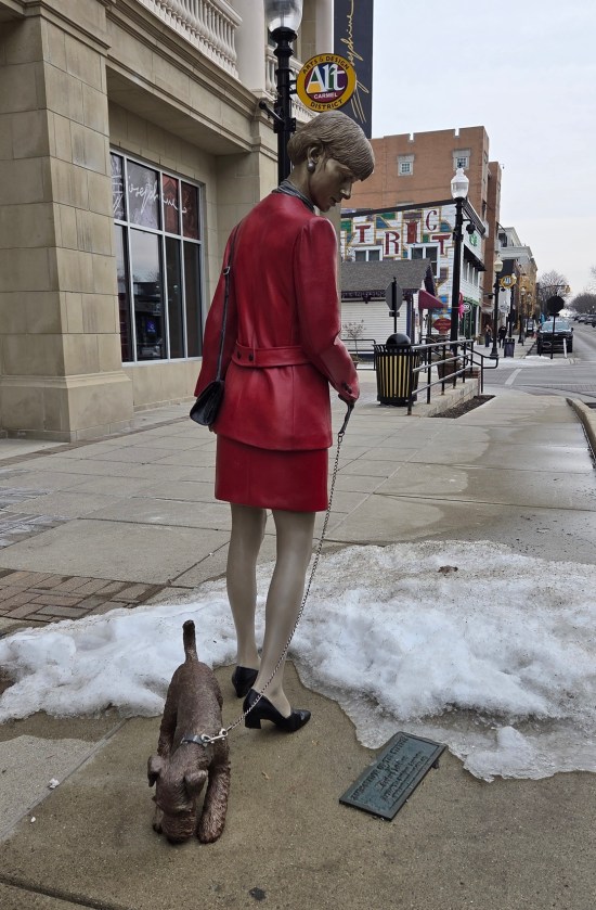 statue of businesswoman dressed in all red walking a sniffing terrier on a leash.