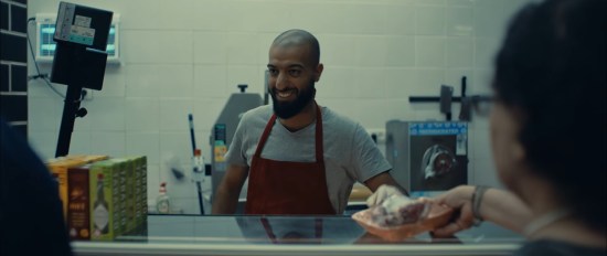 A smiling Palestinian butcher at his counter, greeting happy customers.
