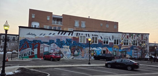 Mural with stylized city, giant piano keyboard floating above it, and the words "art" and "district" worked into the painting.