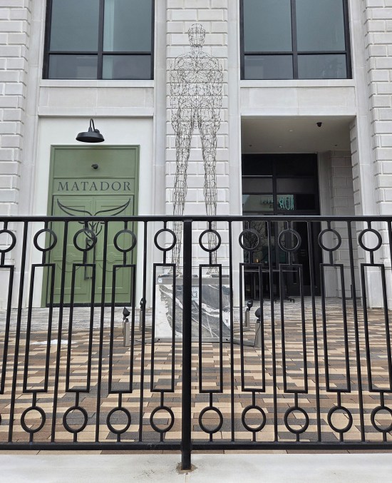 Wire sculpture of a tall faceless male in front of an apartment building called Matador.