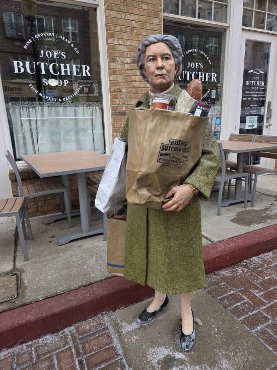 statue of matronly woman with her groceries, positioned in front of an actual butcher shop.