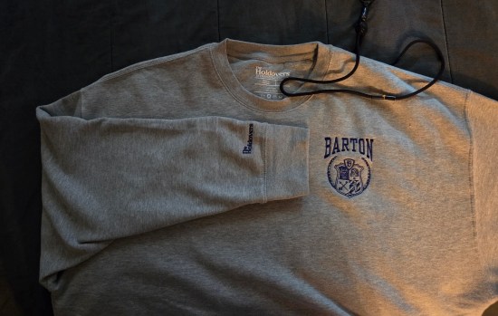 Gray sweatshirt with fictional Barton Academy logo and crest in blue, with "The Holdovers" logo on one sleeve and below the back collar.