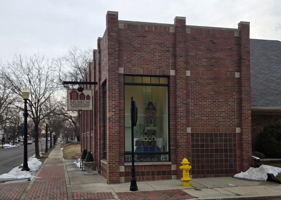 All brick museum with quaint sign hanging out front. Front window has New England-ish dollhouses in it.