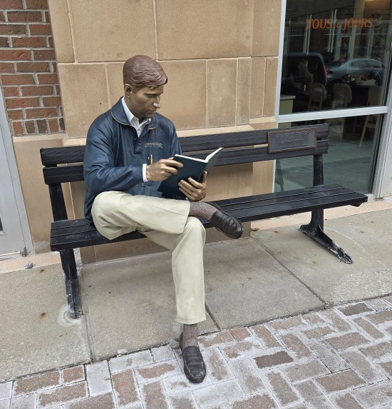 Statue of professional blond guy in a Carmel High School jacket, reading a book on a bench.